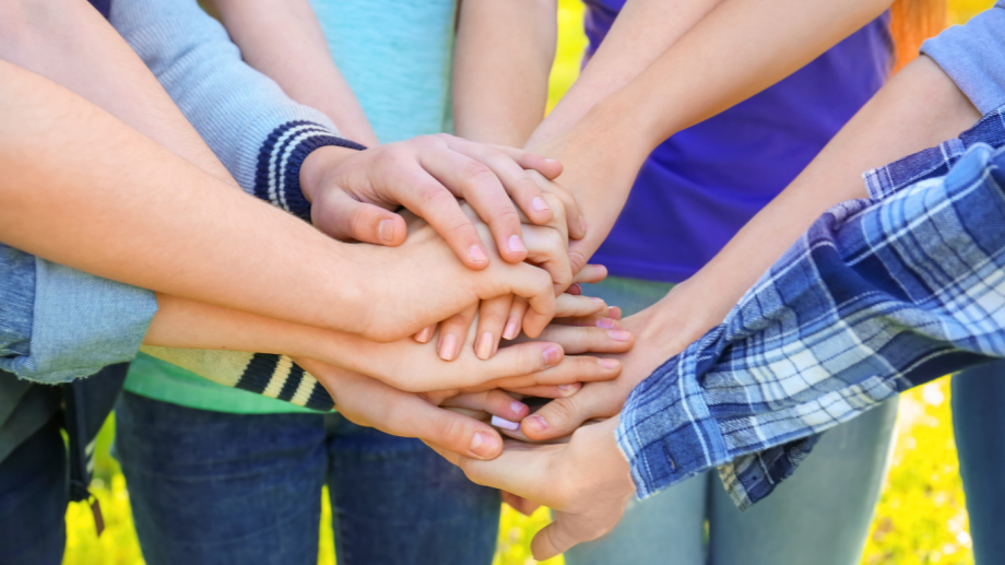 Mehrere Hände verschiedener Menschen liegen als Symbol für Zusammenhalt und Teamwork übereinander.